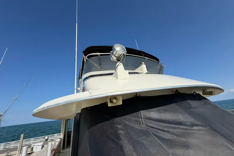 Slide: The Image of 1986 Hatteras 63 Cockpit Motor Yacht docked, showcasing upper deck and radar, under clear blue sky. - 75