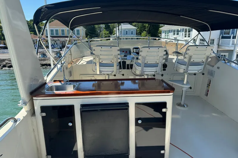 Slide: The Image of 1986 Hatteras 63 Cockpit Motor Yacht helm with seating and sink, docked near waterfront homes. - 60