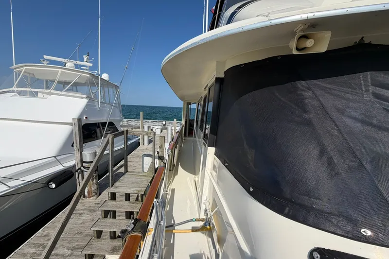 Slide: The Image of 1986 Hatteras 63 Cockpit Motor Yacht docked beside another yacht, clear blue sky. - 73