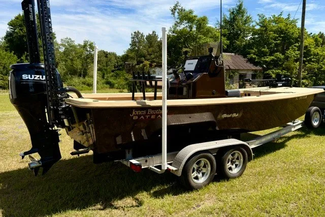 The Image of 2024 Jones Brothers Bateau 20 boat on trailer, featuring Suzuki outboard motor, parked on grass. - 0