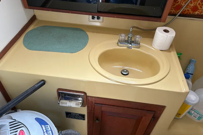 Slide: The Image of 1978 Mainship 34 Trawler bathroom sink with faucet, cabinet, and cleaning supplies. - 30