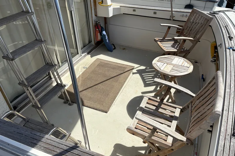 Slide: The Image of 1978 Mainship 34 Trawler deck with wooden chairs and table, featuring a ladder and mat. - 7