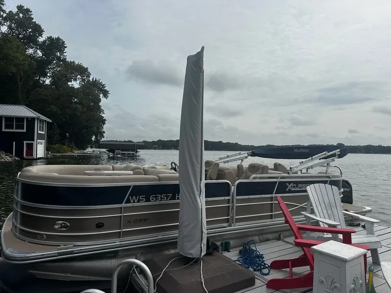 The Image of A 2013 Xcursion 23RF pontoon boat docked. It features beige seating and is surrounded by water. - 2