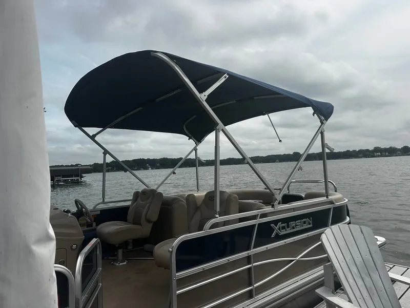 Slide: The Image of A 2013 Xcursion 23RF pontoon boat with a blue canopy, docked on a calm lake. - 0