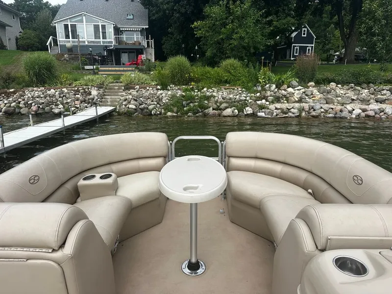 Slide: The Image of A pontoon boat with beige seating and a round table, docked by a lakeside. - 12