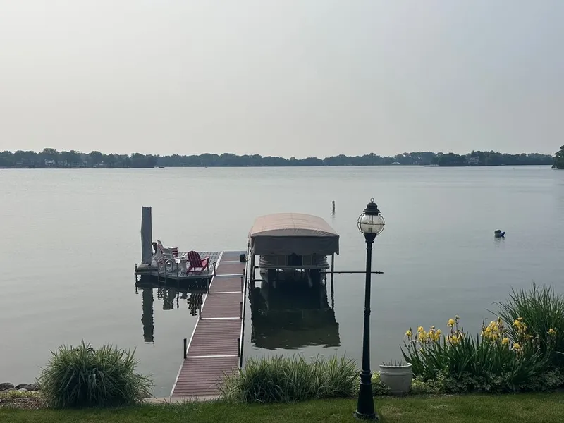 Slide: The Image of A covered boat dock with a boat on it, surrounded by a calm lake and green landscape. - 14
