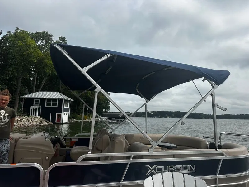 Slide: The Image of A 2013 Xcursion 23RF pontoon boat with a blue canopy, docked by a lakeside. - 16