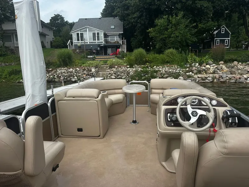 Slide: The Image of A pontoon boat with beige seating and a small table, docked by a calm lakeside. - 6