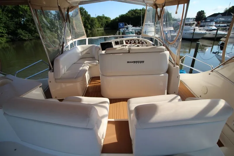 Slide: The Image of 2004 Silverton 410 Sport Bridge yacht interior with white seating and helm, docked by the water. - 16