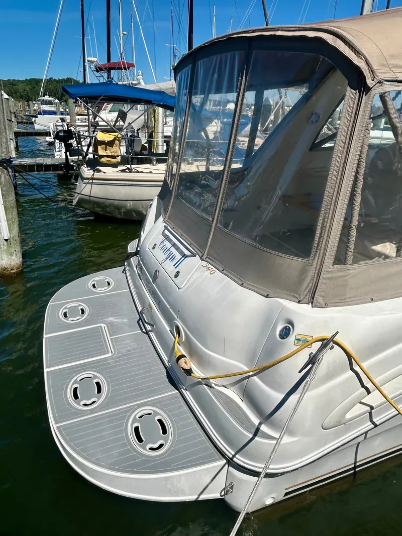 Slide: The Image of A 1999 Sea Ray 340 Sundancer docked in a marina, featuring a beige canopy and spacious swim platform. - 27