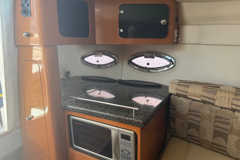 Slide: The Image of 2007 Chaparral 275 SSi boat interior with kitchenette, featuring stove, microwave, and seating area. - 14