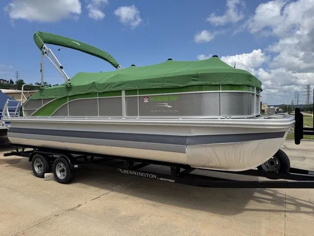 Slide: The Image of A 2022 Bennington 22 SSBX pontoon boat on a trailer, featuring a green cover, parked on a lot. - 2