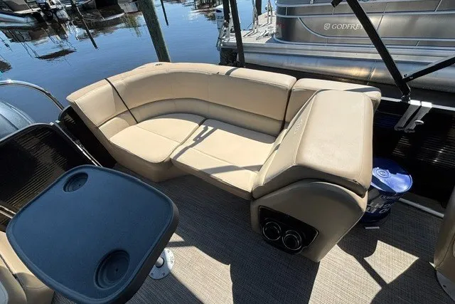Slide: The Image of 2022 Manitou 23 Aurora boat interior with beige seating and table, docked at marina. - 17