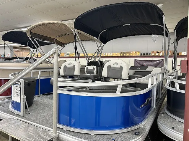 The Image of A blue pontoon boat with black sunshade and white seats is displayed in a showroom. - 1