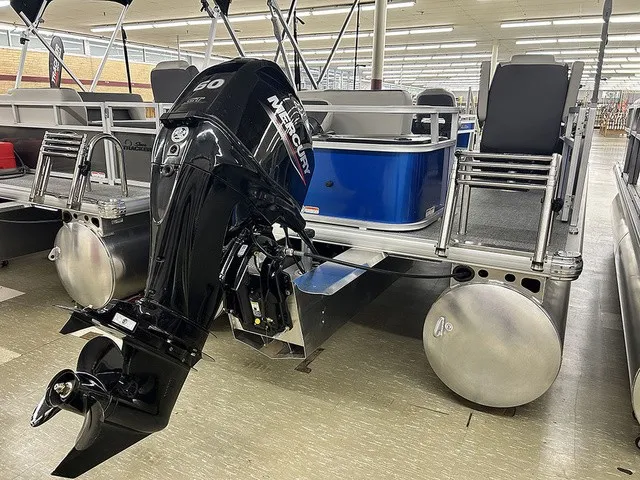Slide: The Image of A Sun Tracker Bass Buggy 18 DLX pontoon boat with a Mercury engine, displayed in a showroom. - 16