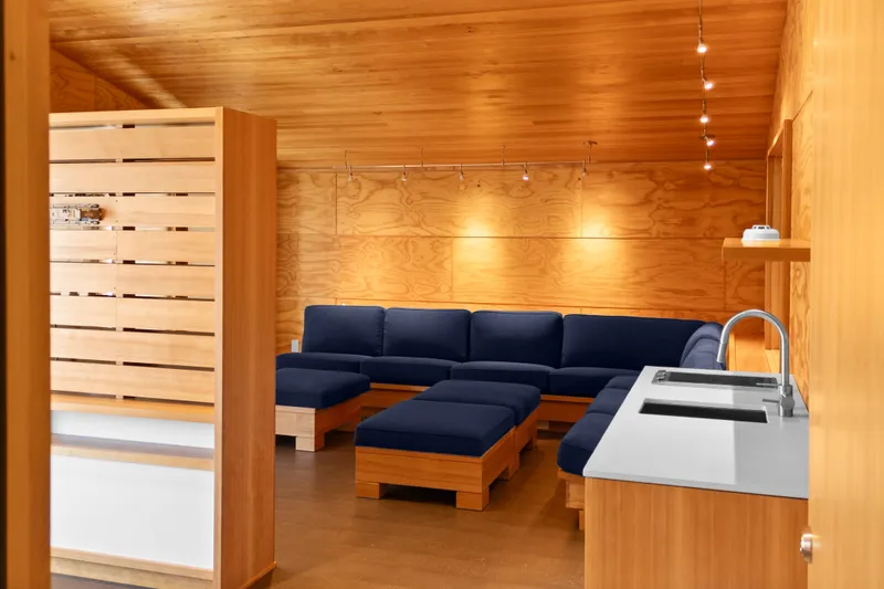 Slide: The Image of Modern boathouse interior with wooden walls, blue sectional sofa, and sleek kitchenette, 1969 design. - 54