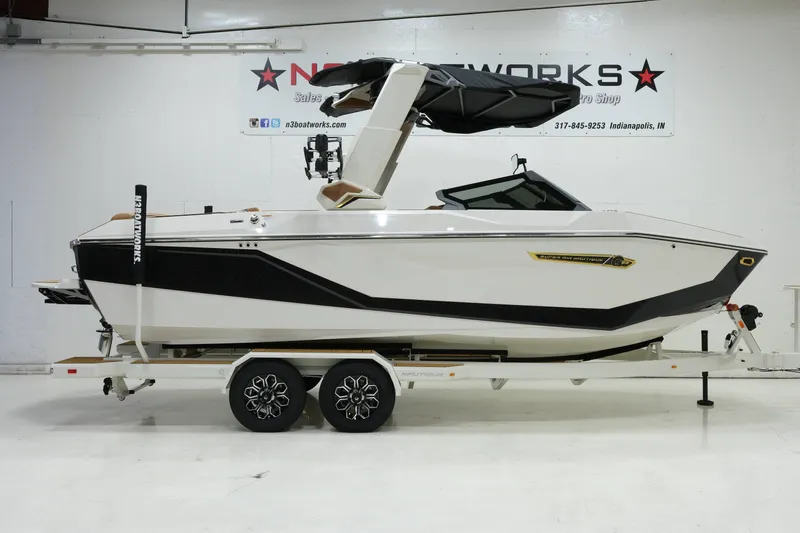 The Image of A white 2027 Nautique G23 boat on a trailer in a showroom. - 1