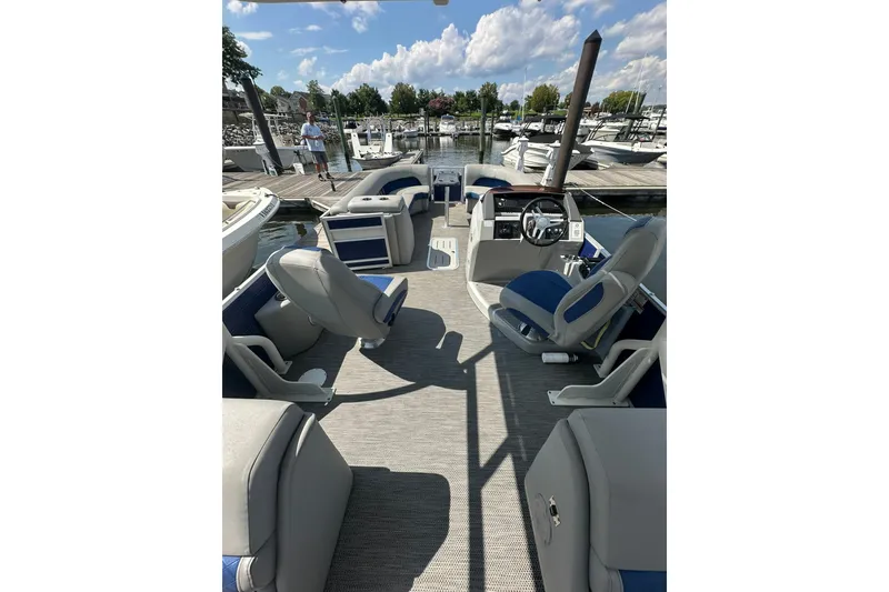 Slide: The Image of 2021 Bennington L Bowrider 25 Swingback interior at marina, featuring plush seating and helm. - 9
