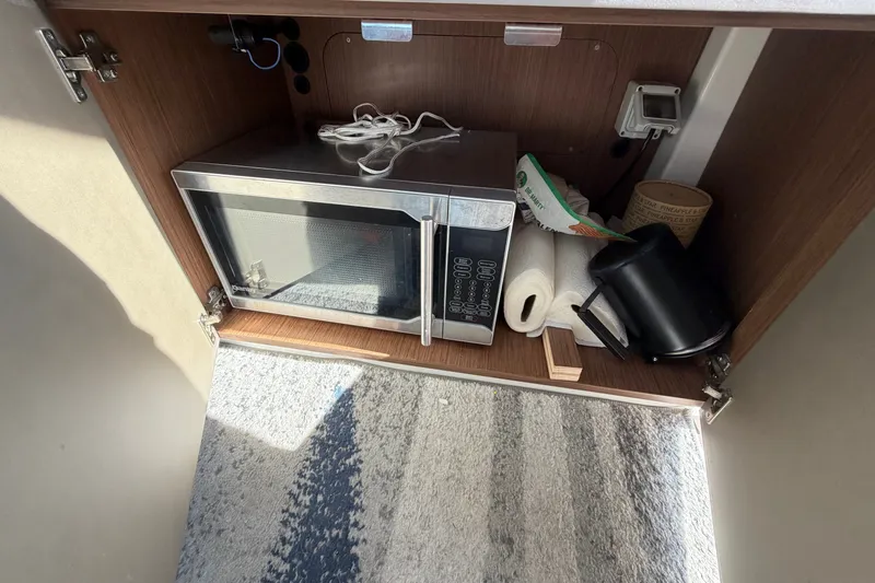 Slide: The Image of Cabinet interior of 2021 Beneteau Antares 27 with microwave and kitchen items. - 28