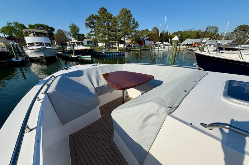 Slide: The Image of 2025 MJM 4 boat with cushioned seating and wooden table in a marina setting. - 43