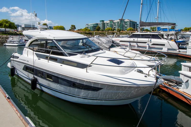 The Image of A 2018 Jeanneau Leader 33 is docked in a marina. It features a sleek design with an enclosed cockpit and large windows. - 0
