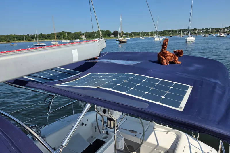 Slide: The Image of Catalina 390 sailboat with solar panels and plush toy on deck, anchored in a scenic harbor. - 26