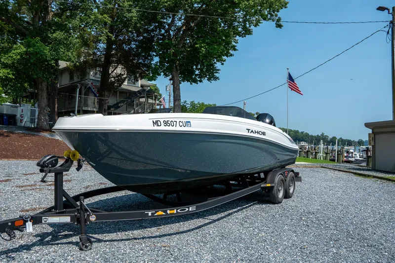 Slide: The Image of 2024 Tahoe T21 boat on trailer, parked near marina with American flag. - 2
