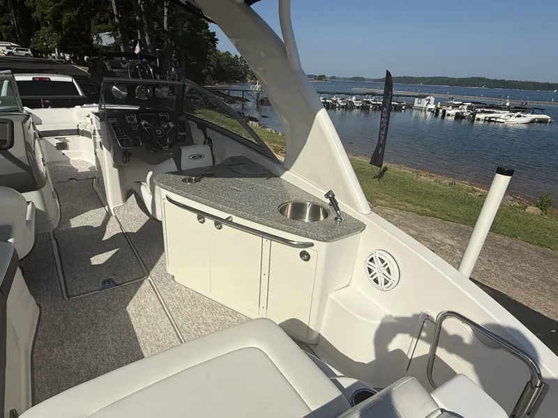 Slide: The Image of The image shows the cockpit of a 2013 Chaparral 264 Sunesta. It features a sink and countertop. A lake with boats is visible in the background. - 19