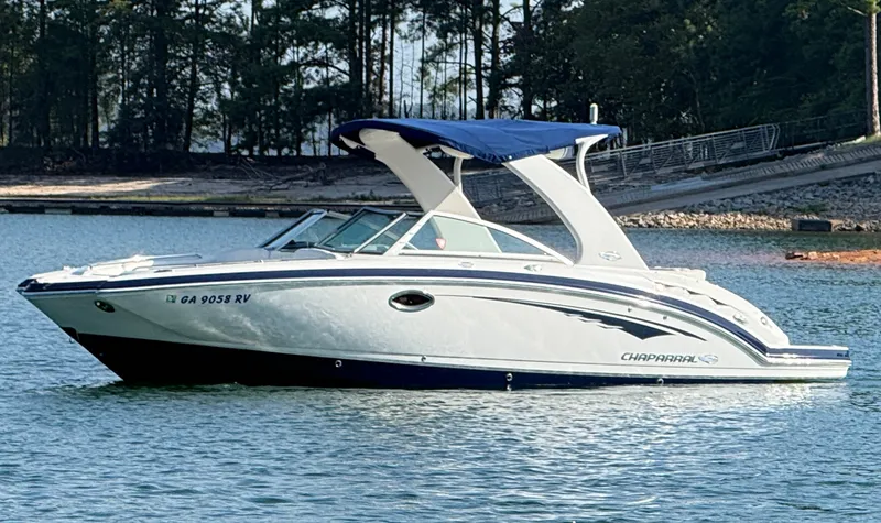 The Image of A white 2013 Chaparral 264 Sunesta boat with a blue canopy on a calm lake. - 1