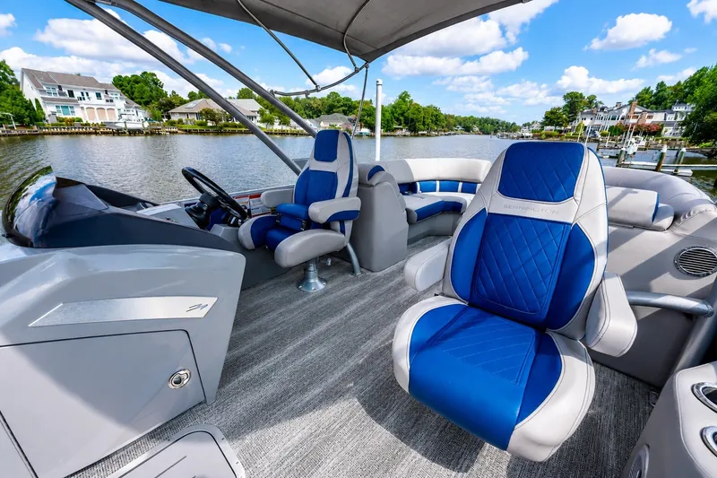 Slide: The Image of 2022 Bennington L 24 Quad Bench pontoon boat interior with blue and gray seating on a scenic lake. - 10