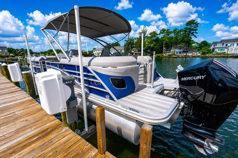 Slide: The Image of 2022 Bennington L 24 Quad Bench pontoon boat docked by a scenic waterfront. - 12