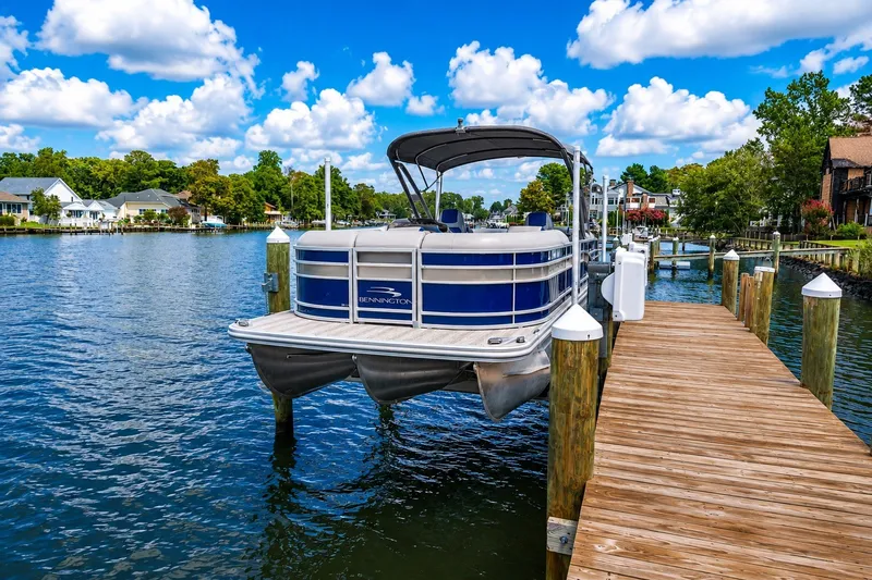Slide: The Image of 2022 Bennington L 24 Quad Bench pontoon boat docked on a sunny lake. - 9
