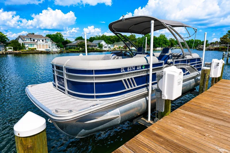 Slide: The Image of 2022 Bennington L 24 Quad Bench pontoon boat docked on a sunny day. - 2
