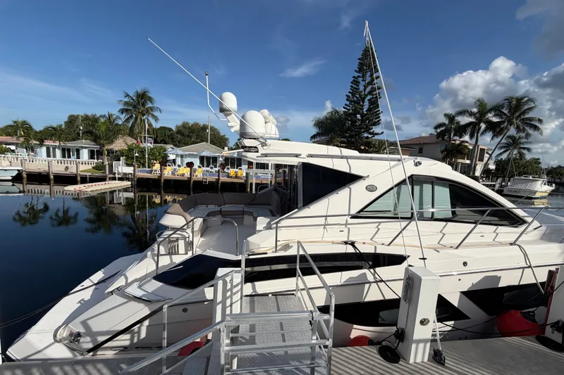 The Image of 2018 Regal 53 Sport Coupe yacht docked by waterfront homes with palm trees. - 5