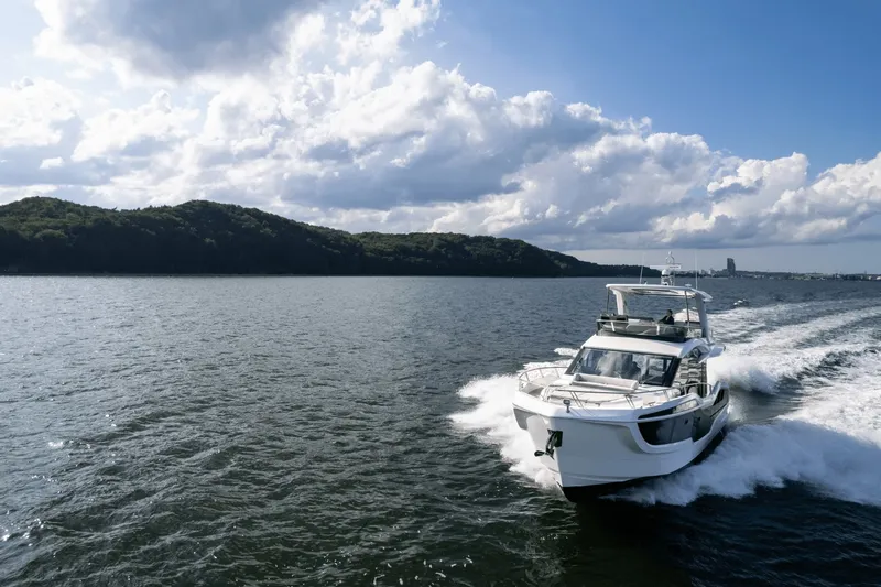 Slide: The Image of Galeon 560 Fly from 2026 cruising on calm waters with wooded hills in the background. - 14