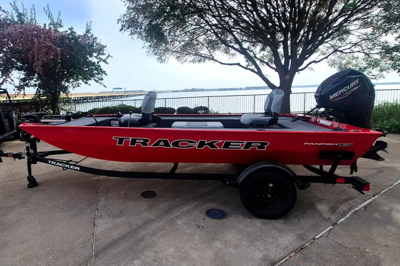 The Image of 2027 Tracker Panfish 17 boat, red, parked near a waterfront with trees in the background. - 0