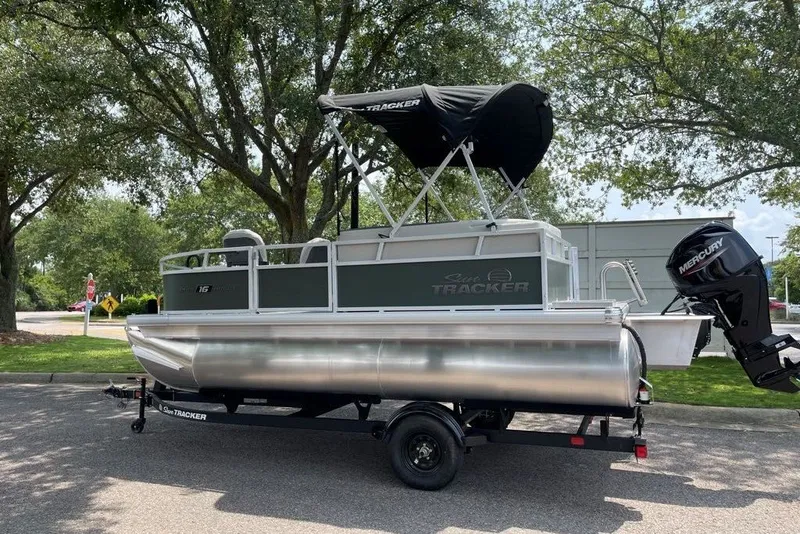 The Image of 2027 Sun Tracker Bass Buggy 16 XL Select pontoon boat on trailer, parked outdoors. - 0