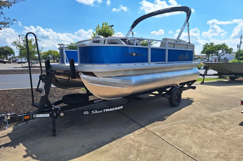 The Image of 2027 Sun Tracker Bass Buggy 16 XL Select pontoon boat on trailer, parked outdoors. - 0