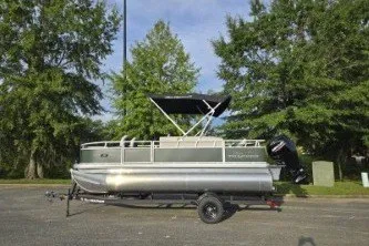 The Image of 2027 Sun Tracker Bass Buggy 18 DLX pontoon boat on trailer, parked outdoors. - 0