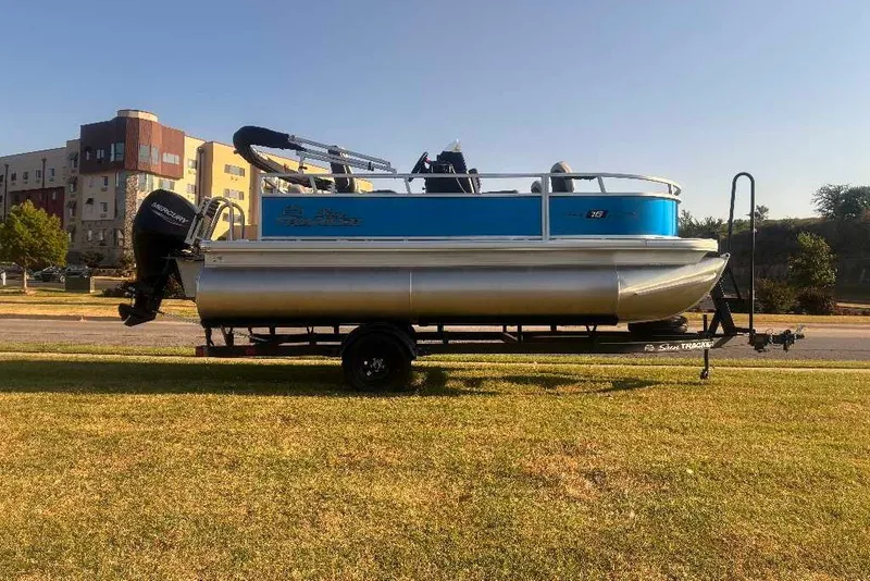 The Image of 2027 Sun Tracker Bass Buggy 16 XL Select pontoon boat on trailer, parked on grass. - 0