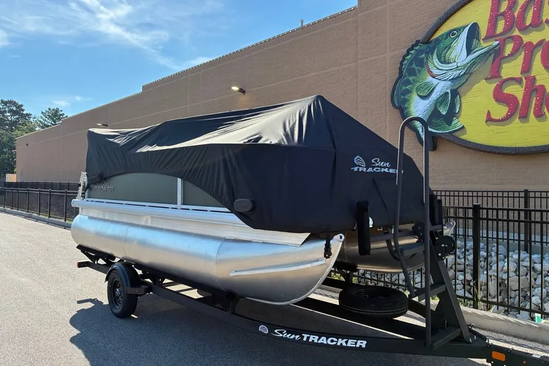 Slide: The Image of 2027 Sun Tracker Bass Buggy 16 XL Select pontoon boat covered, parked outside Bass Pro Shops. - 19
