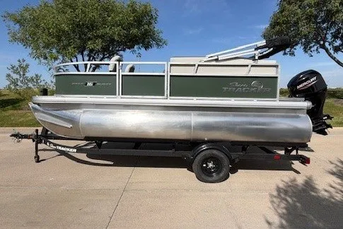 The Image of 2027 Sun Tracker Bass Buggy 16 XL Select pontoon boat on trailer, parked outdoors. - 1