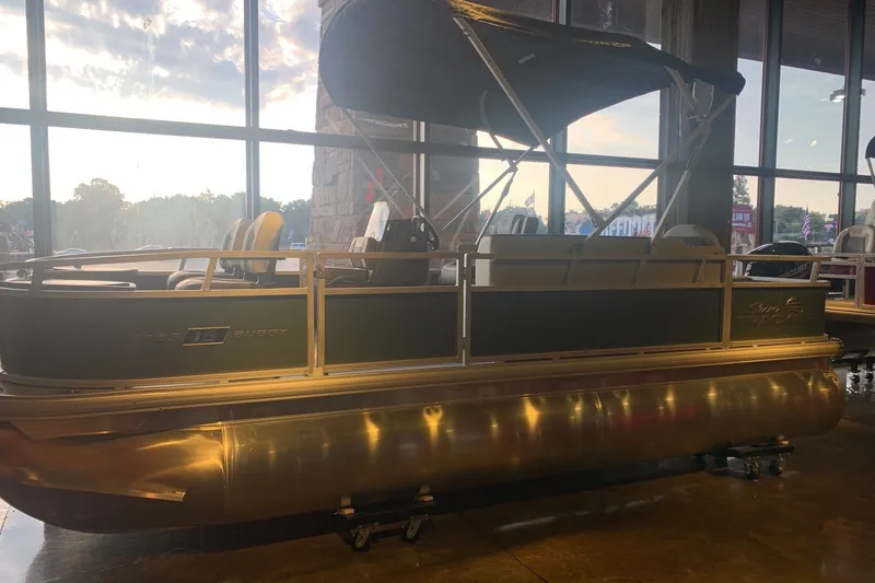 The Image of 2027 Sun Tracker Bass Buggy 18 DLX pontoon boat displayed indoors at sunset. - 0