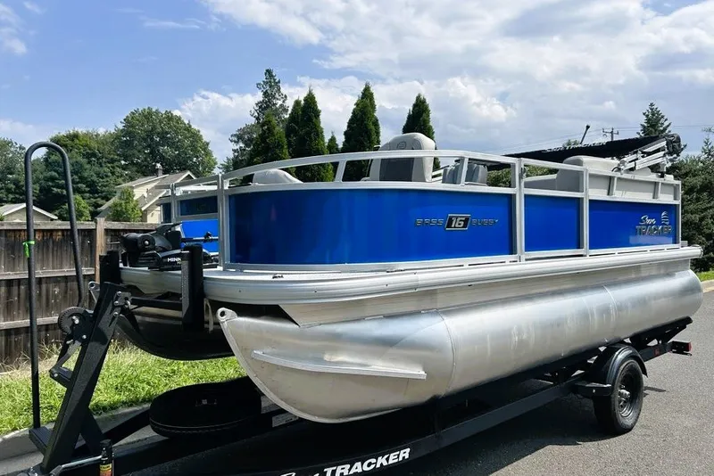 The Image of 2027 Sun Tracker Bass Buggy 16 XL Select pontoon boat on trailer, parked outdoors. - 0