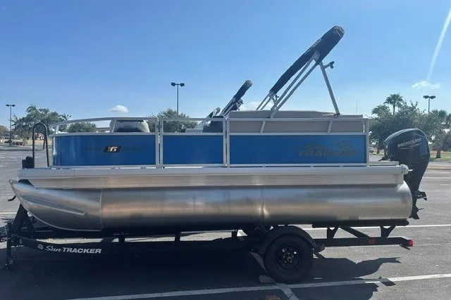 The Image of 2027 Sun Tracker Bass Buggy 16 XL Select pontoon boat on trailer in parking lot. - 0