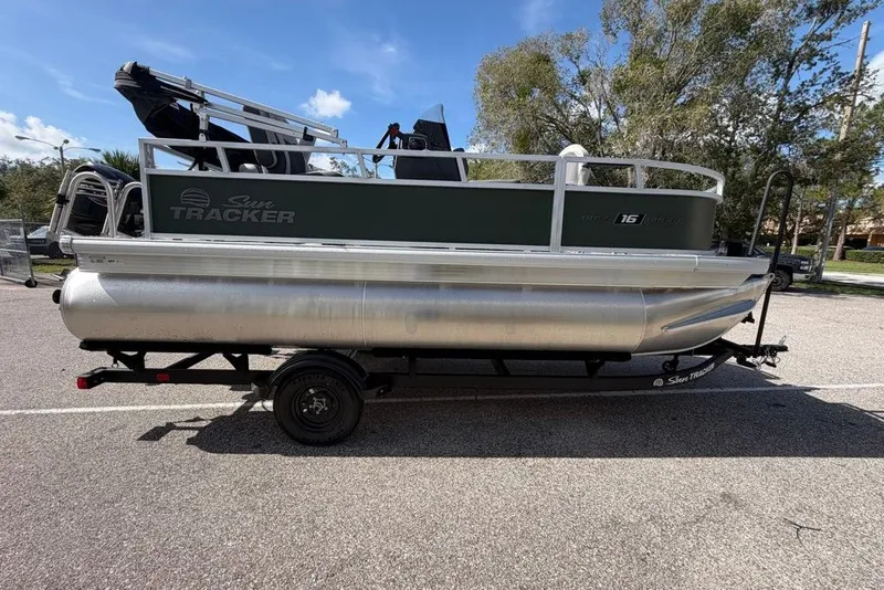 The Image of 2027 Sun Tracker Bass Buggy 16 XL Select pontoon boat on trailer in parking lot. - 0