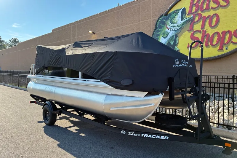Slide: The Image of 2027 Sun Tracker Bass Buggy 18 DLX pontoon boat covered, parked at Bass Pro Shops. - 18