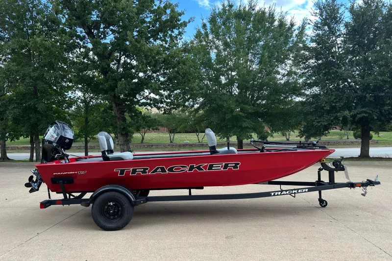 Slide: The Image of Red 2027 Tracker Panfish 17 boat on trailer, parked outdoors with trees in background. - 17