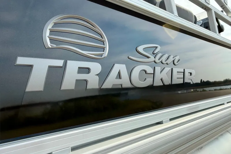 Slide: The Image of 2027 Sun Tracker Bass Buggy 18 DLX logo on boat exterior, near water. - 16