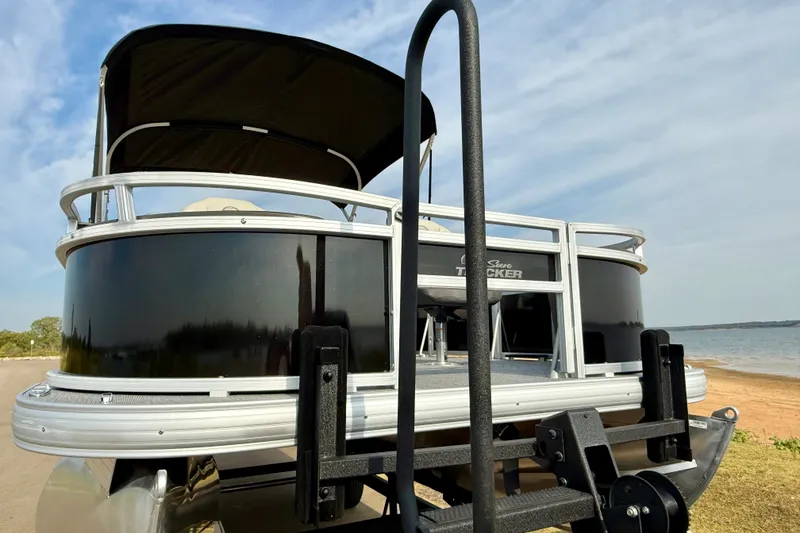 Slide: The Image of 2027 Sun Tracker Bass Buggy 18 DLX pontoon boat on trailer by a lakeside. - 20